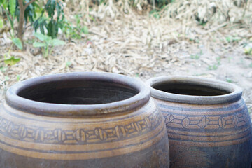 Fototapeta premium Two traditional clay jars placed outdoors on ground, showcasing rustic pottery containers used for water storage or fermentation, highlighting cultural heritage and simple rural lifestyle.