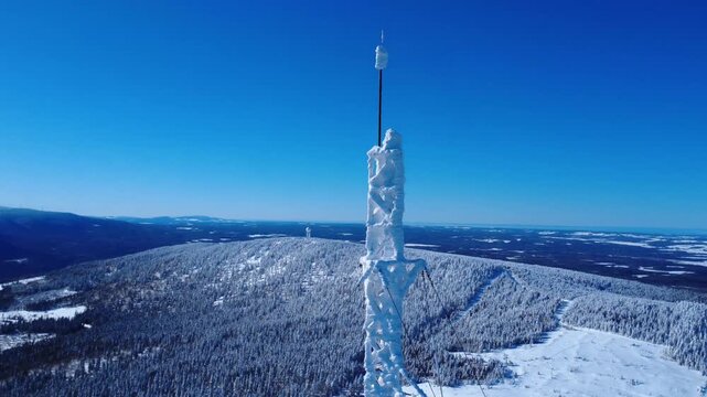 Aerial drone shot of an icy communication tower and distant Doppler radar on a snowy Quebec mountain. Breathtaking winter panorama of the Matapedia Valley under a clear blue sky. Canada 2026.