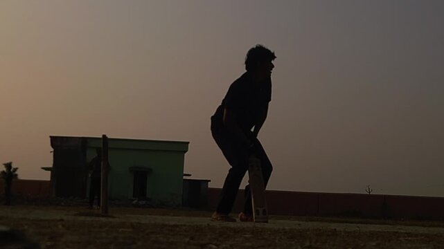 Silhouette of a cricket player holding a bat in a batting stance during sunset on an outdoor field. Ideal for cricket, sports training, fitness, youth sports, recreation, motivation