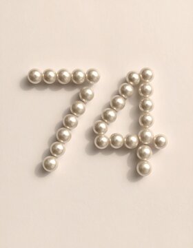 Number 74 made out of small pearls on a neutral solid background