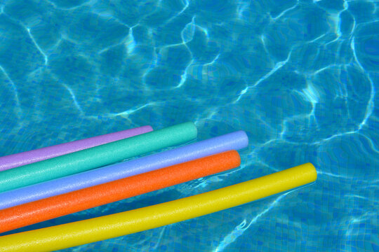 Colourful pool noodles floating on water in swimming pool