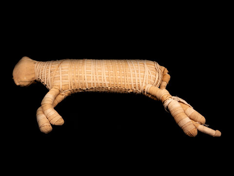 Mummified cat wrapped in linen bandages from Ancient Egypt, used as a votive offering (sacrifice). Ptolemaic period (332 to 30 BCE). Isolated on a black background.