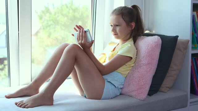 A little girl of European appearance is using a smartphone. The kid is playing virtual games or watching cartoons on her smartphone. The child with a smartphone. The problem of addiction to gadgets