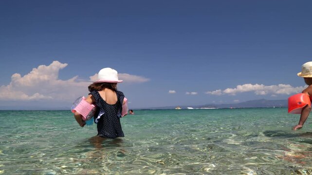 Video of two young children standing in clear shallow sea water with inflatable armbands on a sunny summer beach.