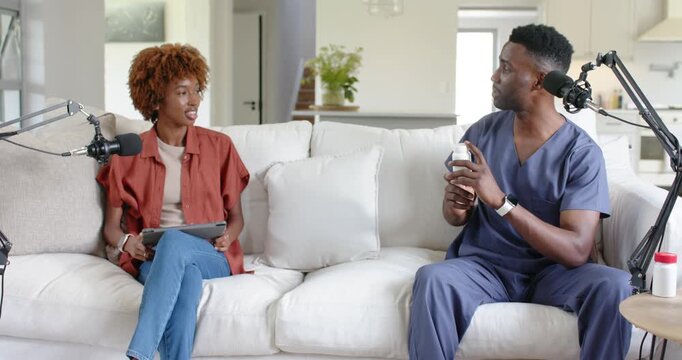 African American host and guest on couch, checking tablet, guest in scrubs showing bottle with mics