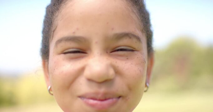 African American teenage girl facing camera, reacting, leaning forward, smiling in park with hoops