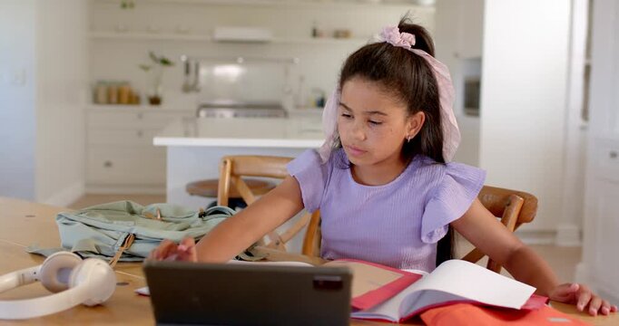 African American preteen girl seeing tablet flipping red folder sorting papers at kitchen table