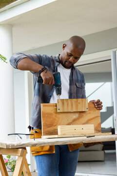 African American man drilling and assembling wood frame on front porch using cordless drill