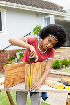 Following plan, homeowner measuring plywood panels, steadying panel, preparing cuts for shelf