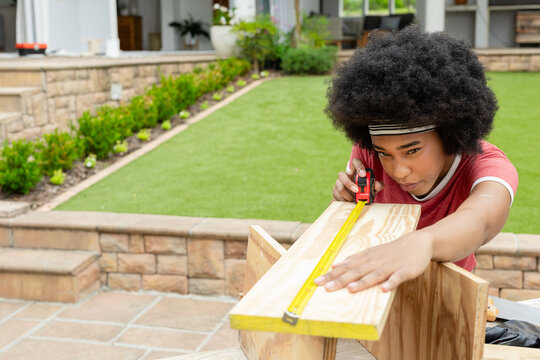 Measuring woman aligning tape measure in red shirt over pine board on tiled patio, copy space