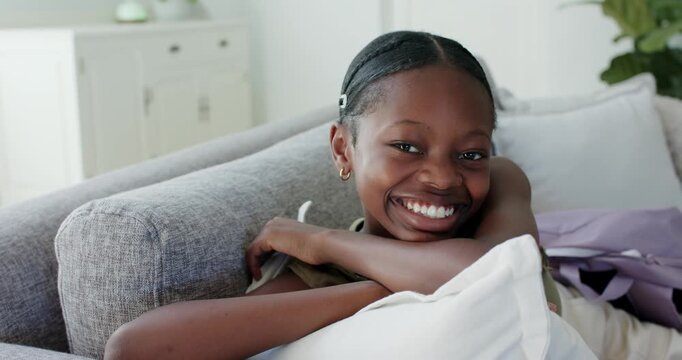 Pre-teen girl noticing camera reclining on gray sofa holding white cushion tilting head and smiling