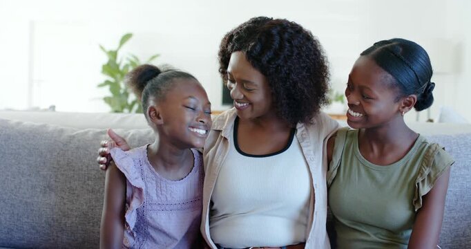 Laughing left child starting chat, mother hugging girls in jeans on living room sofa, plant bonding
