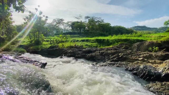 Beautiful view of rocky fast flowing river and lush green fields under clear sky