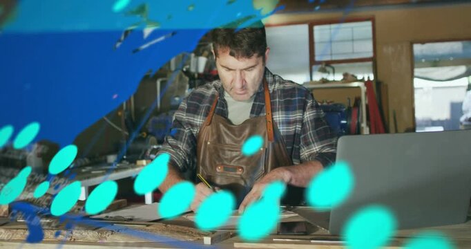 Man drafting and measuring on woodshop bench as laptop sending data overlaying plans, refining plan