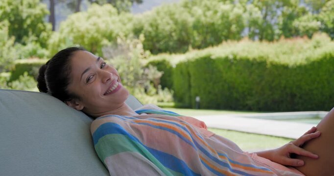 African American woman reclining on pool lounger, opening eyes toward camera and adjusting coverup