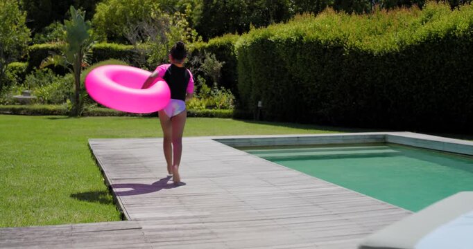 African American mother and daughter, mother placing hand, encouraging her into pool with pink ring
