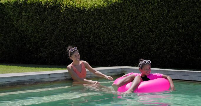 African American mom steadying pink ring as child drifting, guiding kicking at pool teaching swim