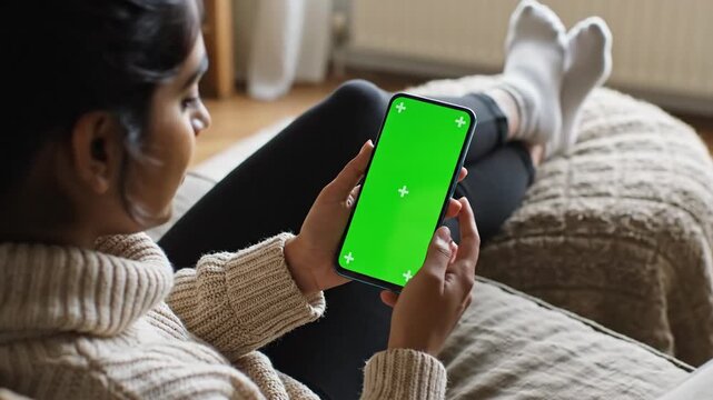 Person relaxing with smartphone featuring green screen for content insertion