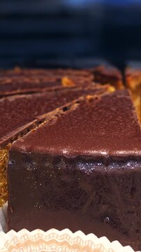 Slices of a rich and decadent chocolate cake, possibly a sacher torte, resting on a tray in a bakery display case, tempting customers with its glossy ganache and moist sponge