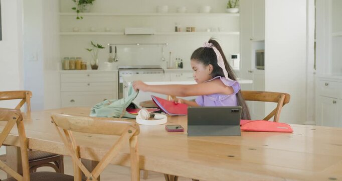 African American child packing light green backpack at dining table tablet, red folder, copy space