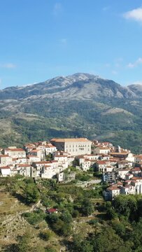 Scenic aerial view of the historic hilltop village of Aieta with traditional stone houses and red roofs, surrounded by lush green mountains in southern Italy.