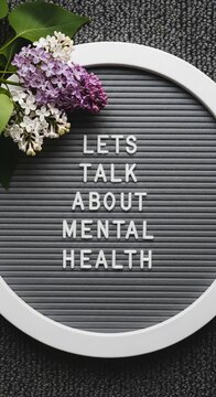 Mental health awareness message on grey letter board, lilac flowers on circular felt board, lets talk about mental health concept for wellness