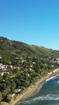 Aerial view of the picturesque coastline and hillside village of Acciaroli, Italy, with lush greenery and blue sea under a clear sky.