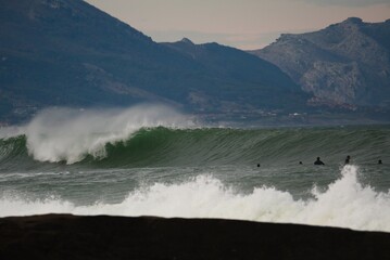 A breathtaking image of a large wave poised to crash against a rocky shoreline, capturing the raw power of nature and the calmness of the surroundings at dusk. © Aperezer