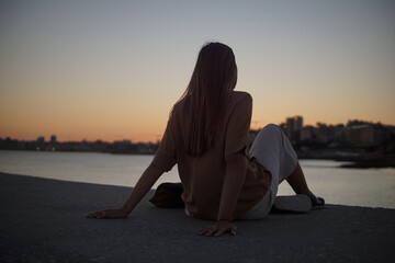 A serene silhouette of a woman sitting by the water during sunset, reflecting on tranquility and the beauty of nature, creating a peaceful ambiance in the scene. © Aperezer