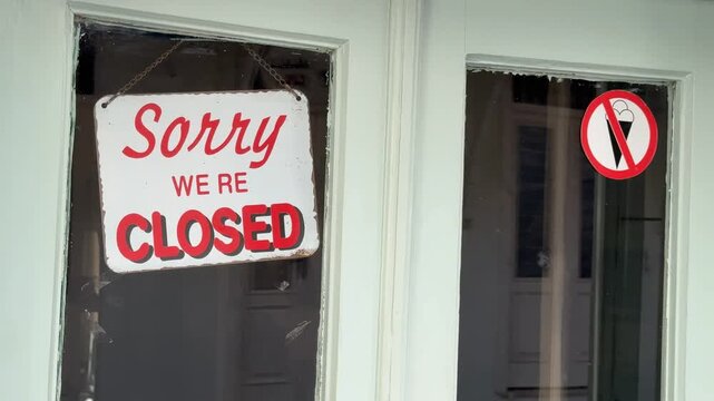 Closed sign hanging on a door with ice cream prohibition sticker during business hours closure