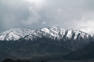 Obraz premium Snowy rugged dramatic mountain peak landscape cloudy sky winter cold remote natural outdoor scenic wilderness highland rocky serene tranquil majestic adventure