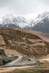 Naklejka premium Winding road mountain snow landscape travel adventure nature scenic remote transportation. winding road curves through remote mountain landscape with snow capped peaks background evoking sense