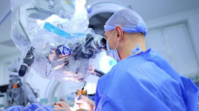 Caucasian neurosurgeon sits at the microscope. Rear view. Doctor applies carefully the surgical tools at operation.
