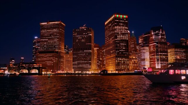 Illumination from high-rises at the waterfront reflects in the river. A cruise boat passes by during night tour.