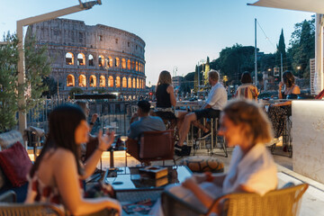 Plakat Unrecognisable people enjoy drinks with a view of the Colosseum in Rome at dusk.