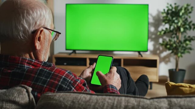 Senior adult relaxing watching tv with green screen and holding phone