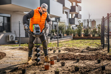 Gardener using tools hand-held soil hole drilling machine or portable manual cordless earth auger for prepare the soil for planting plants. © Peter