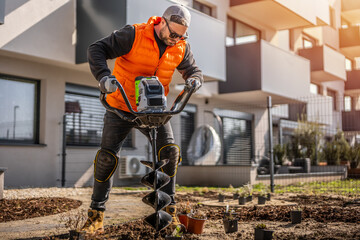 Gardener using tools hand-held soil hole drilling machine or portable manual cordless earth auger for prepare the soil for planting plants. © Peter