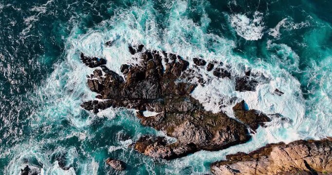 Top down aerial view of white surf on rocks. Factual top view of turquoise pacific ocean water and waves breaking on rocky shoreline in Big Sur, California.