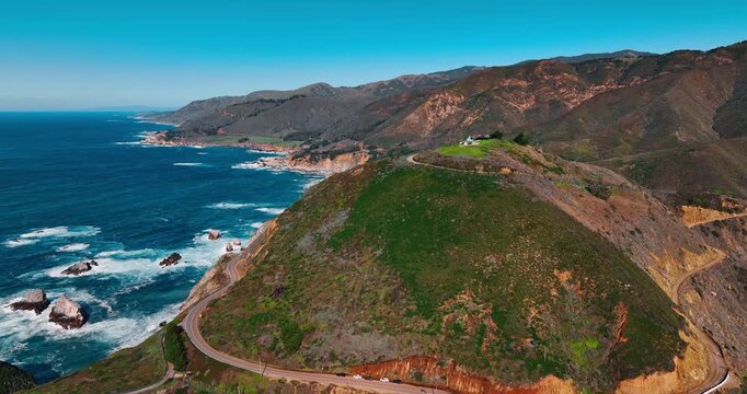 Aerial view of hairpin turn on coastal highway. High angle shot of a sharp road curve on a green hill overlooking the pacific ocean in Big Sur, California.