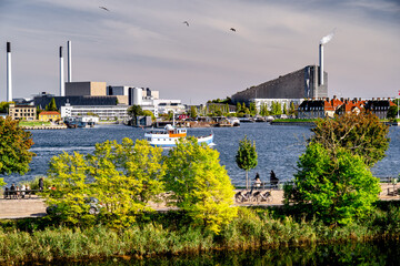 Obraz premium Panorama Copenhagen waterfront with smokestacks and ship and people on promenade, Denmark.