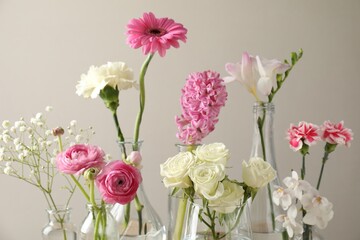 Fototapeta premium Beautiful flowers in vases against light background, closeup