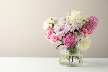 Fototapeta premium Bouquet of beautiful flowers in vase on white table against light background. Space for text
