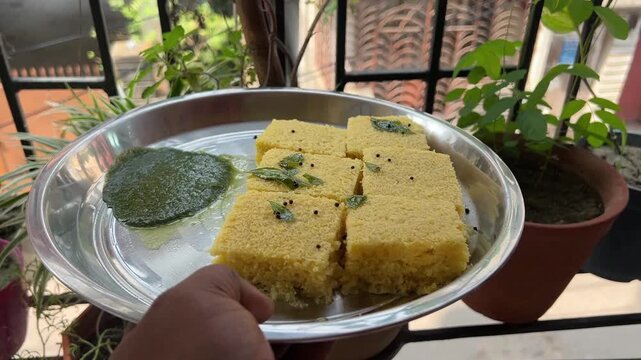 Freshly prepared spongy Khaman Dhokla: a traditional steamed savoury chickpea flour cake garnished with mustard seeds and green chillies.