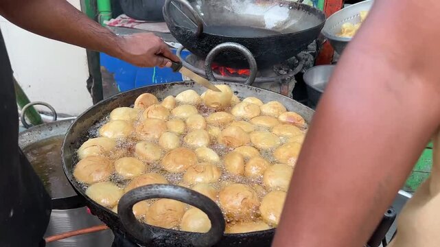 Sizzling street food: A local Indian dhaba cook deep-frying spicy Khasta Kachoris in a large iron wok (kadai) filled with bubbling oil.