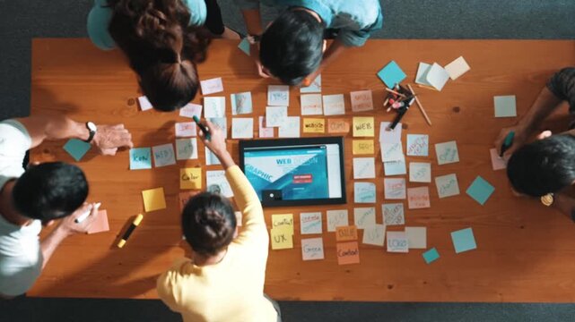 Top down view of programmer brainstorming and planning about web design while looking at tablet wireframe prototype. Aerial view of skilled developer team talking about digital application. Symposium.