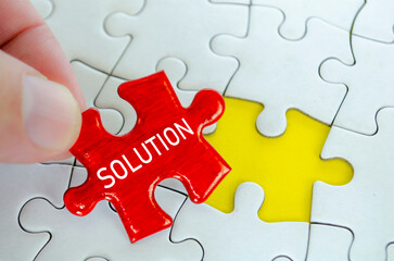 Fototapeta premium Red solution puzzle piece being placed by hand beside a yellow piece on a white jigsaw puzzle background.