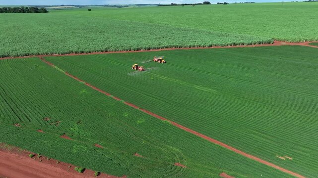 Aerial view of a tractor spraying green peanut crops next to a vast sugarcane plantation