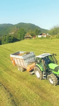 Aerial fly away while tractor loading grass on silage trailer in mountains