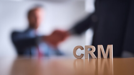 Fototapeta premium Shiny block letters for customer relations management concept rest on a polished desk with a blurry business handshake in background